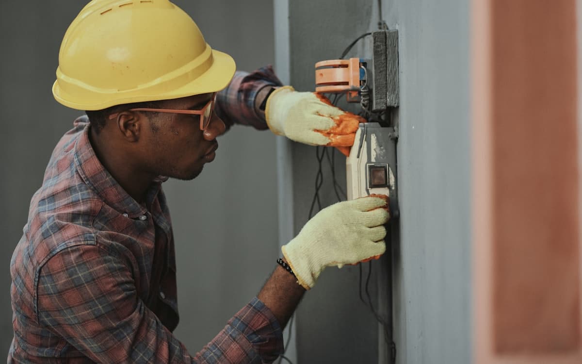 An electrician in a hard hat wiring a switchboard